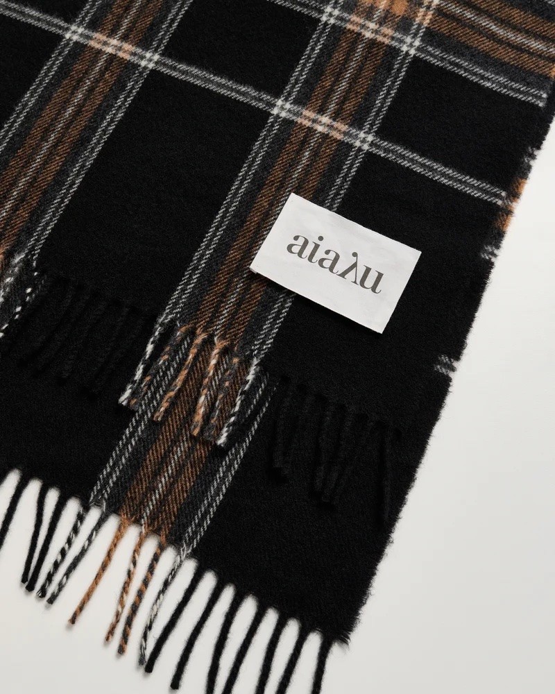 Close up af Aiayu Kaya Scarf Mix Black ternet uld halstørklæde med frynser og Aiayu logo